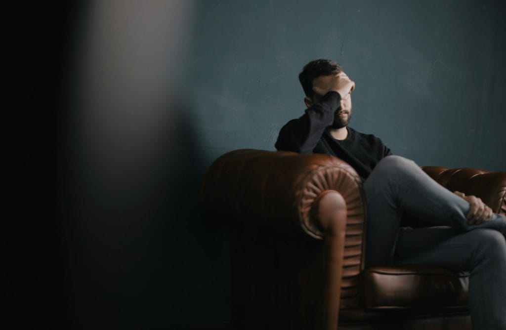 Person sitting in a leather chair with head resting in one hand, appearing distressed or overwhelmed.